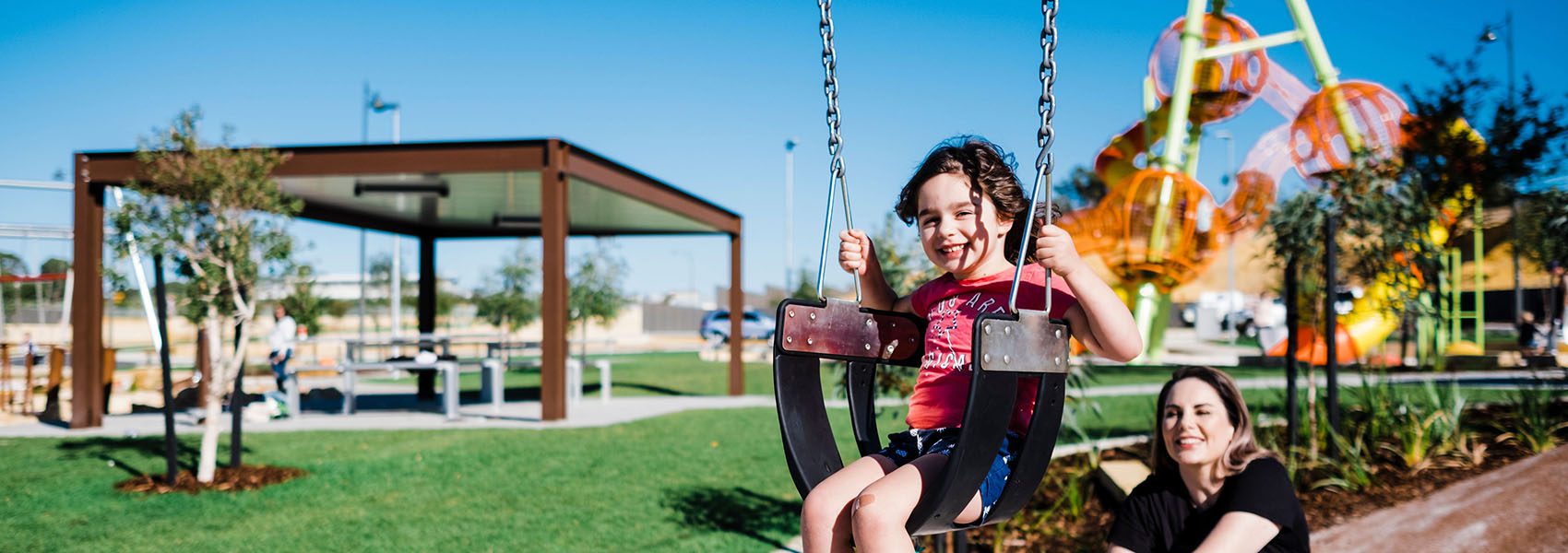 This image shows a child having fun on the swing at Brightwood Park in Baldivis. There is bright green grass and fun equipment to play with. Move Homes has house and land packages in Baldivis near Brightwood Park.
